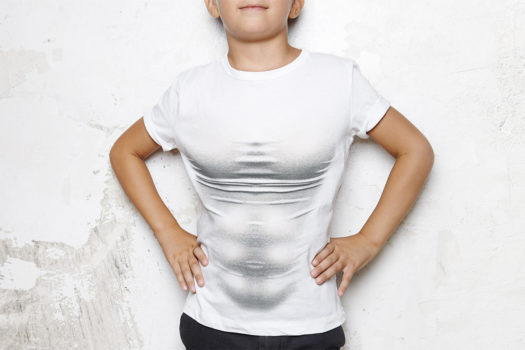  Boy wearing white tshirt, shorts and glasses, stands on a wall background and smiling
