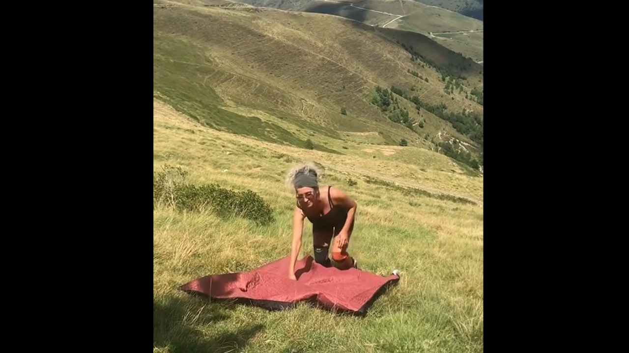 Cette dame tente d'étendre sa nappe en pleine montagne, mais rien ne se passe comme prévu